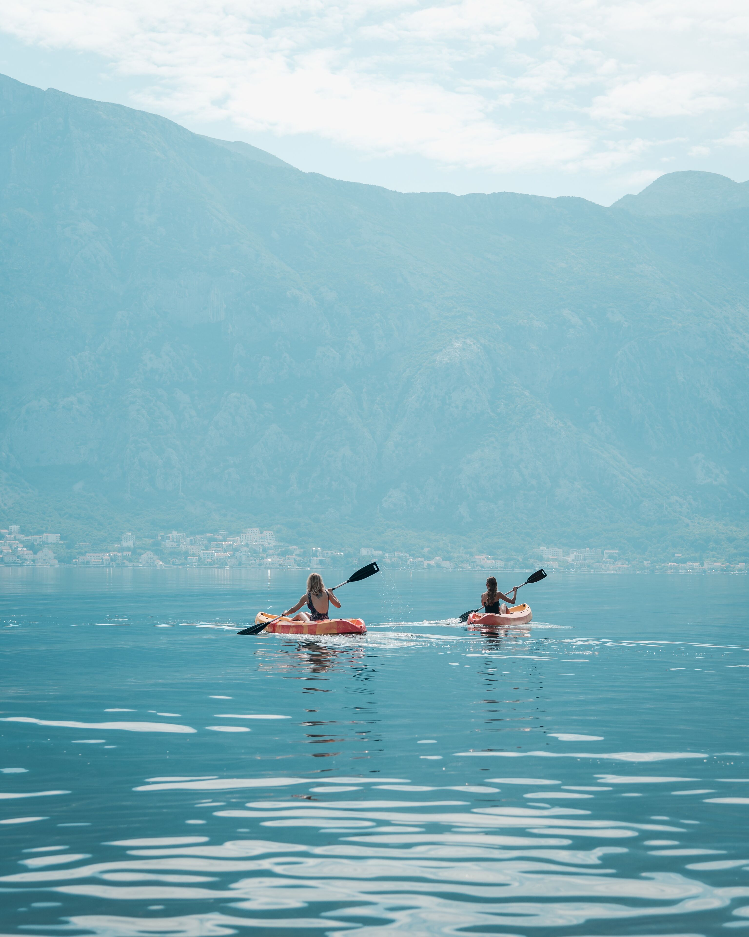 Deux personnes pratiquent le kayak sur un lac paisible, avec des montagnes en arrière-plan.
