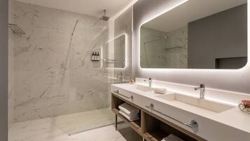 A modern bathroom with marble walls, a large mirror, dual sinks, and a shower area.
