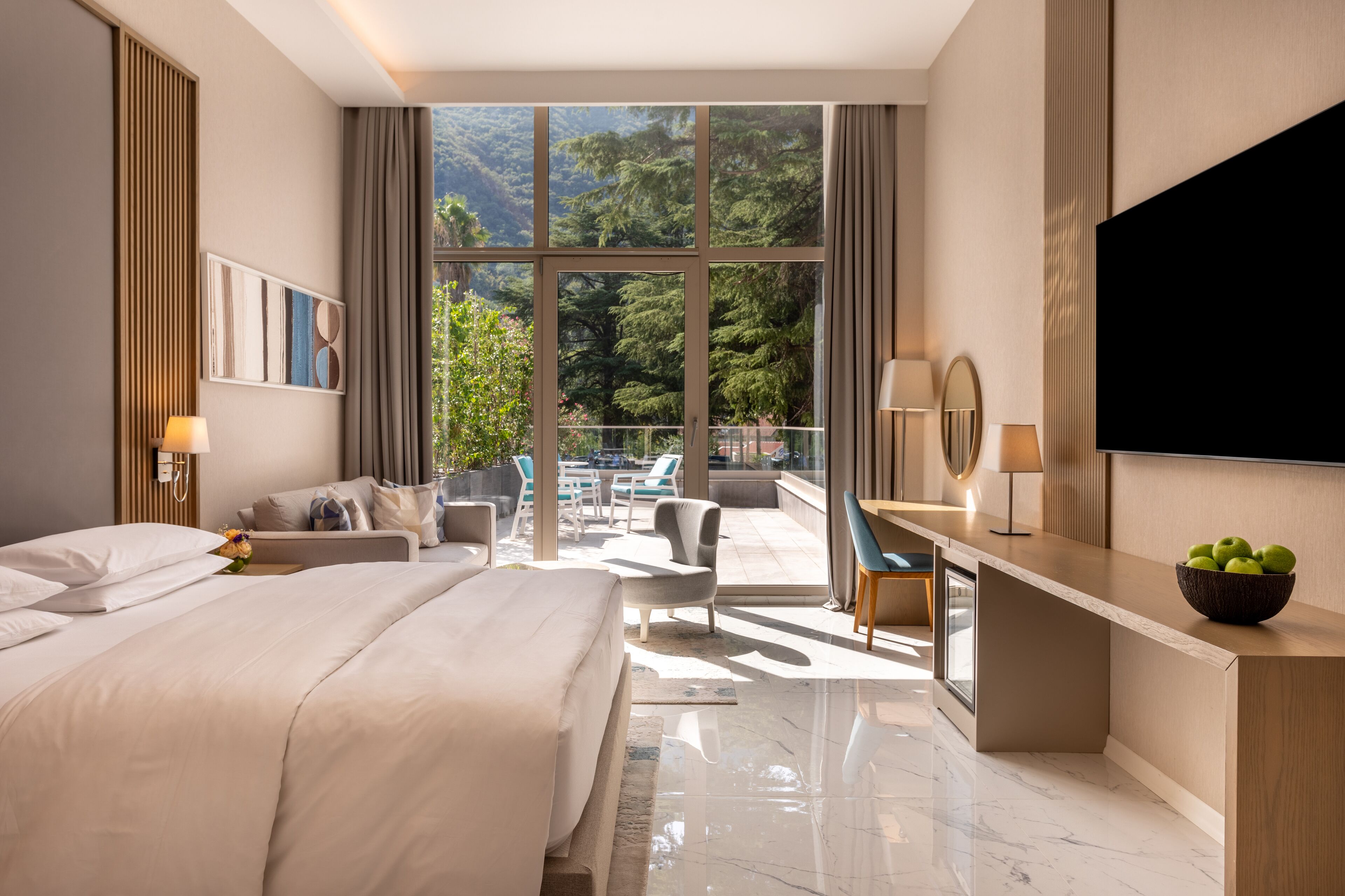 Una habitación de hotel moderna con una cama grande, un escritorio, un televisor y un balcón con vistas a las montañas.