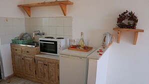 A compact kitchen with a Bosch oven, a sink, and a small refrigerator. There is a wooden shelf with a decorative wreath and a coffee maker. - Gongis Studios (Corfu)