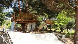 A hammock suspended between two trees in a wooded area with wooden structures. - Gongis Studios (Corfu)
