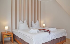 Un lit bien fait, avec des oreillers, une lampe de chevet et une pile de serviettes sur une table de chevet en bois.