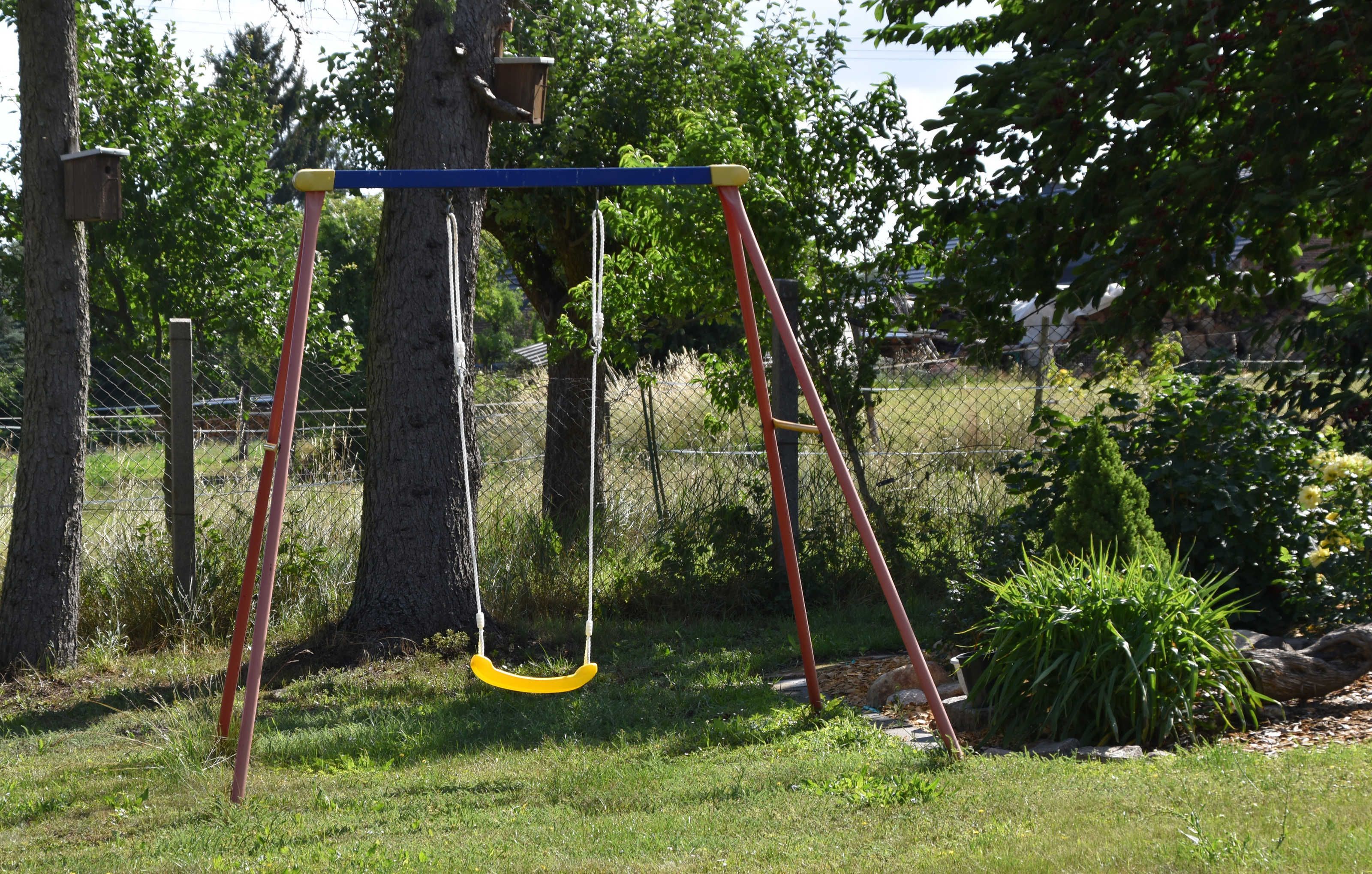 A swing set in a grassy area with trees and a fence in the background.