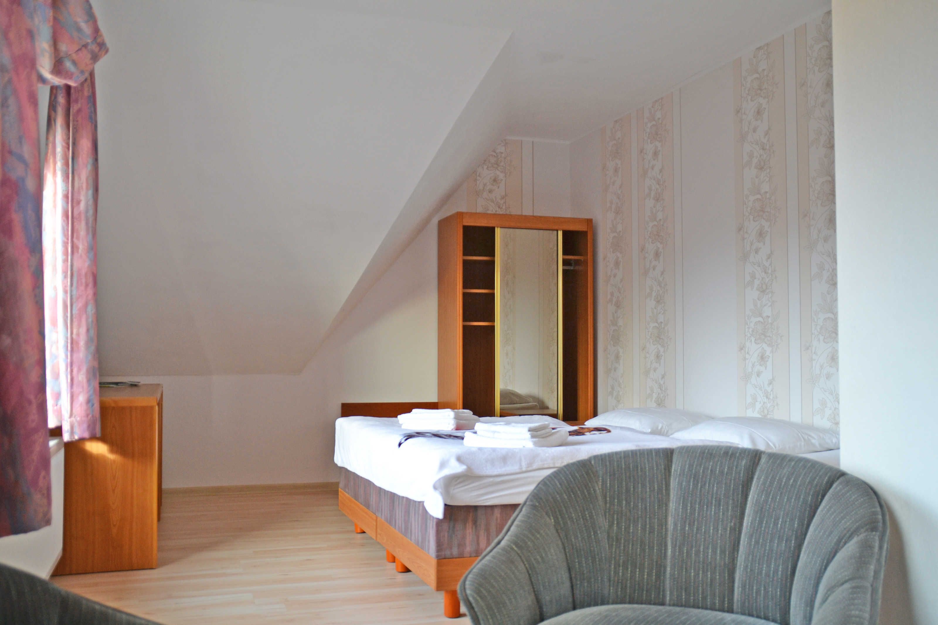 A bedroom with a bed, a chair, a wooden cabinet, and a large mirror.