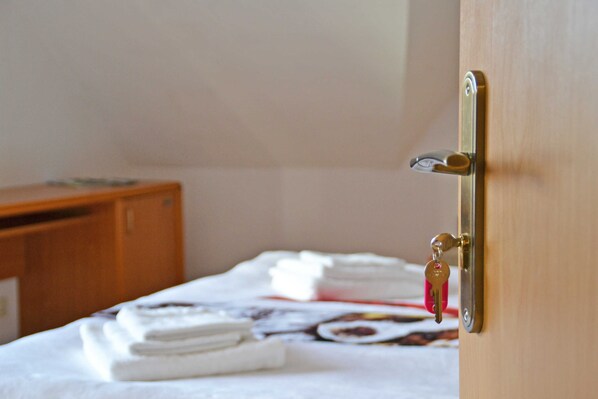 A hotel room with a bed, a wooden dresser, and a door with a key in the lock. - Apartment Wiesenblick - Apartment (Schenkendöbern)