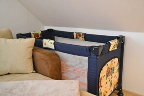 A room with a bed, a sofa, and a baby playpen with a mesh top and colorful fabric sides. - Apartment Wiesenblick - Apartment (Schenkendöbern)