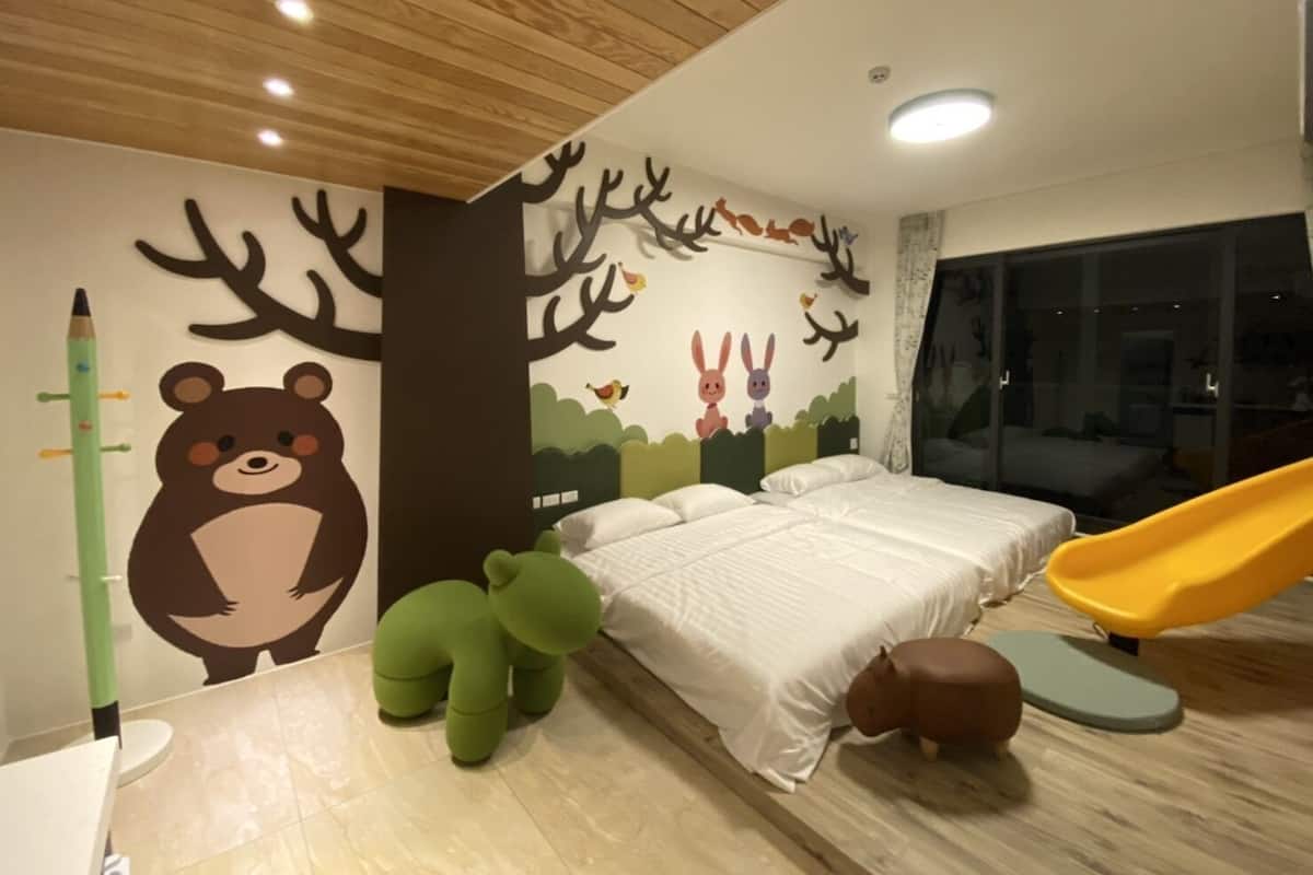 A child's bedroom with a bed, a slide, and playful wall decorations including a bear, rabbits, and trees.