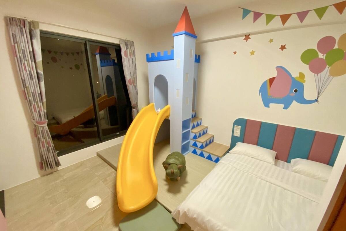 A child's playroom with a slide, a castle play structure, and a bed with a colorful headboard.