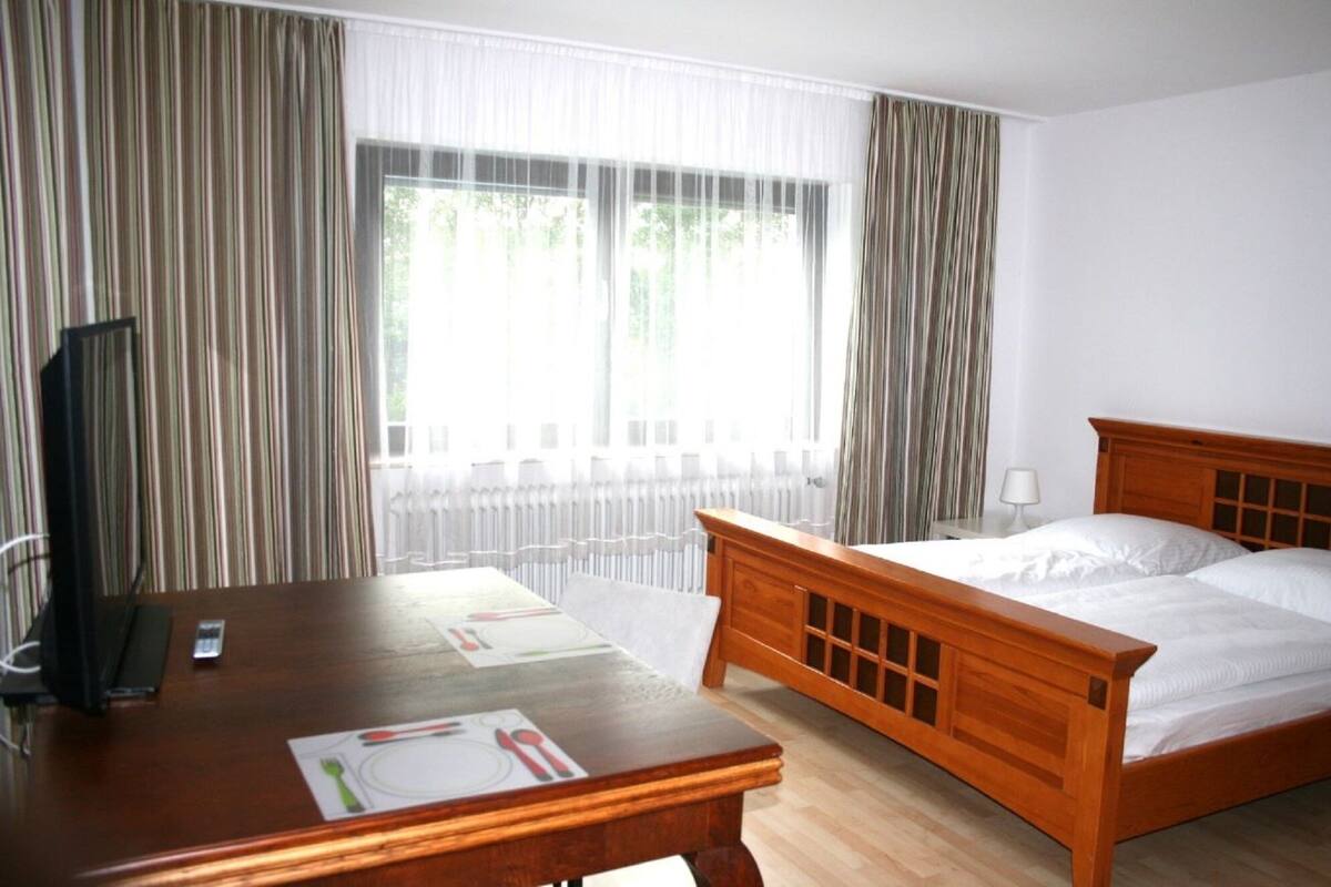 A hotel room with a wooden bed, a desk with a chair, a television, and a window with curtains.