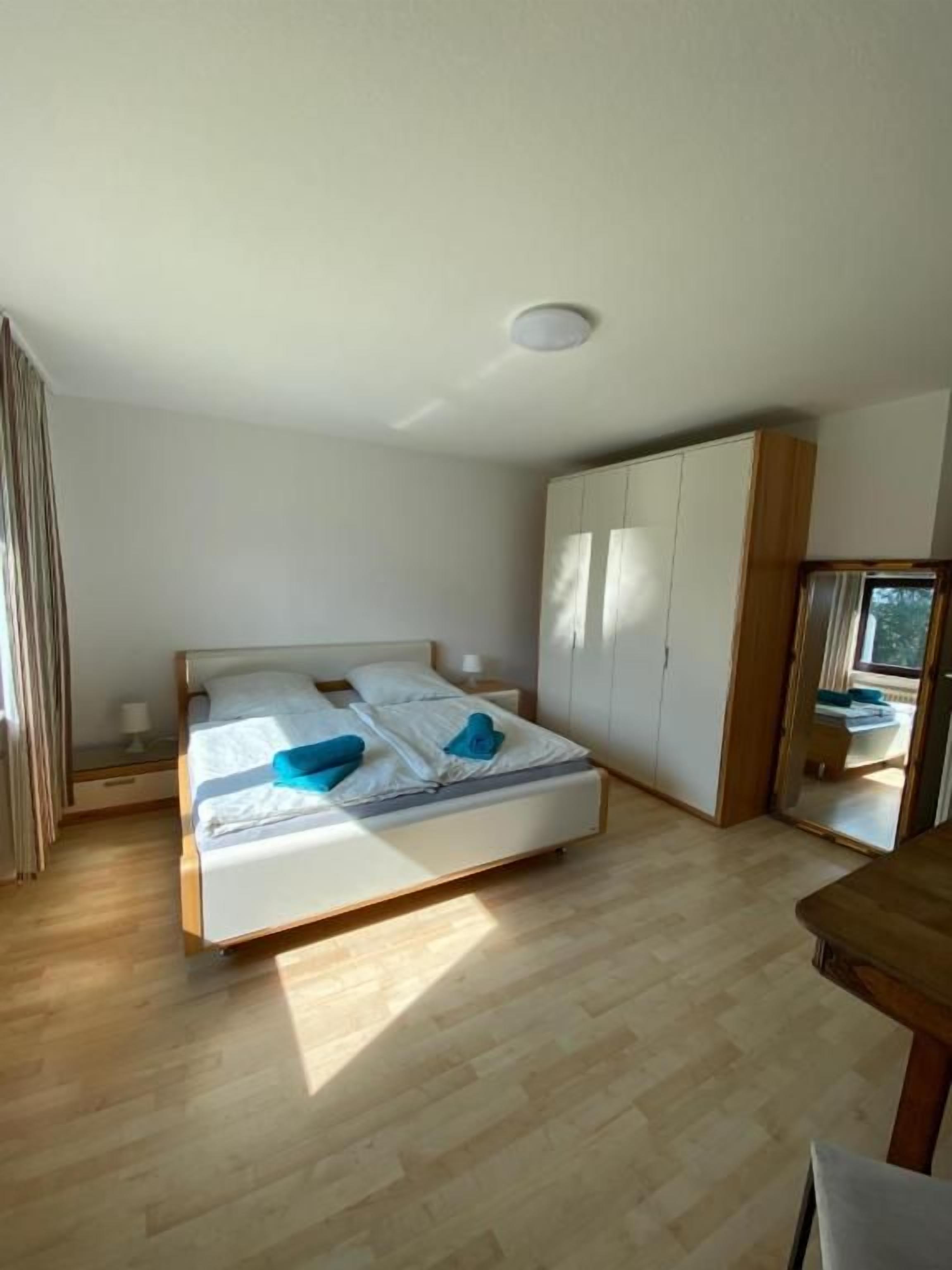 A bedroom with a bed, wooden floor, wardrobe, and a window.