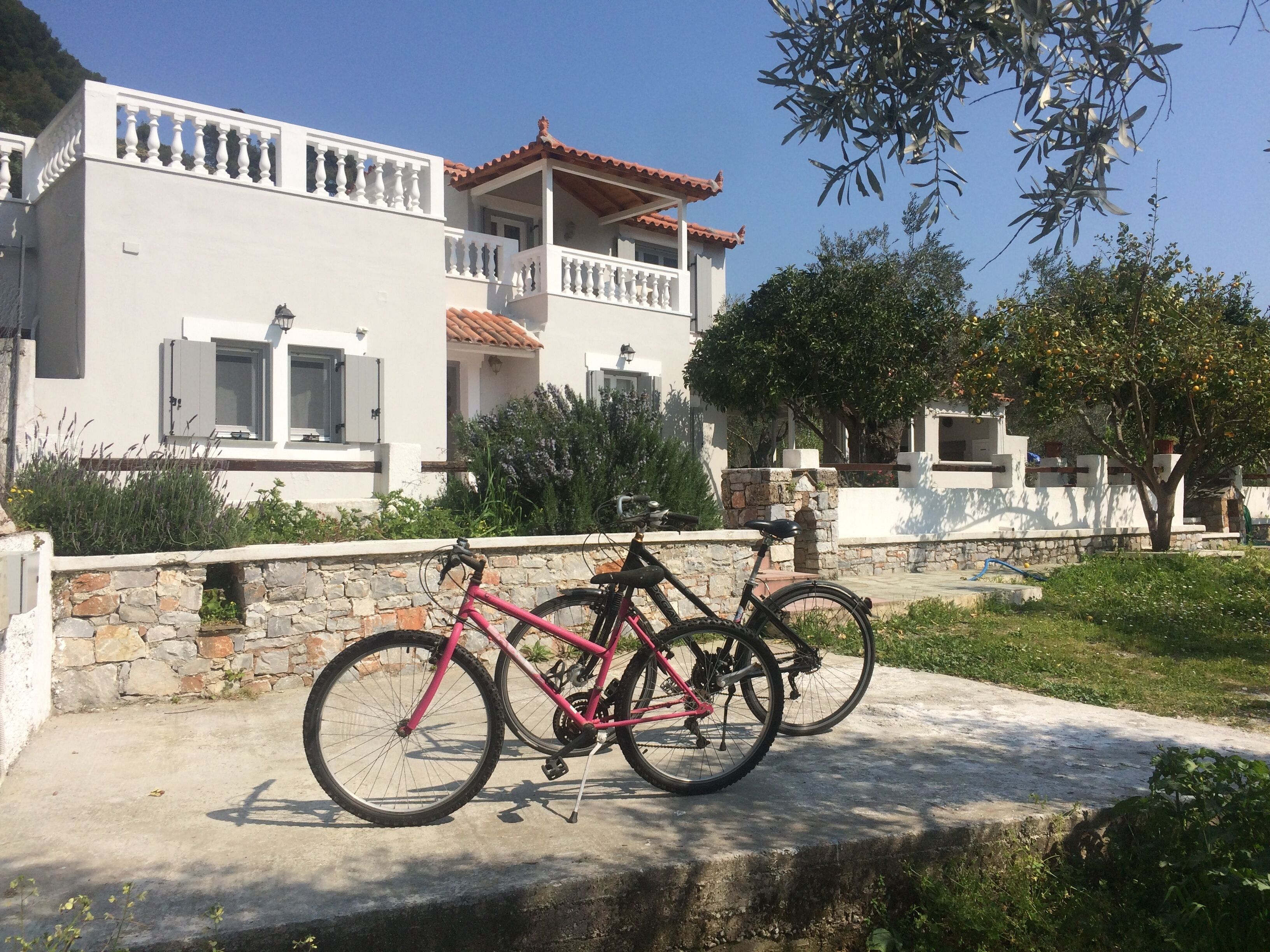 Un bâtiment blanc avec un balcon, un v élo rose et un mur de pierre.
