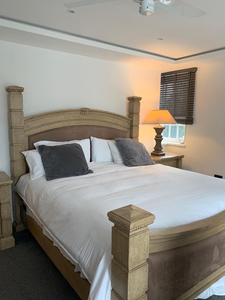 A bed with a wooden headboard, a bedside table with a lamp, and a window with blinds.