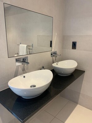 A modern bathroom with two white sinks, a large mirror, and a black countertop. - Regency House (Esher)