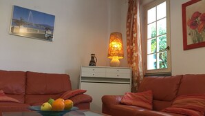 A living room with two brown leather sofas, a glass coffee table with a bowl of fruit, a white cabinet, a lamp, and a window with curtains. - Casa Matilde (Massa)