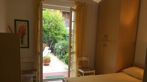 A bedroom with a bed, a chair, a wardrobe, and a view of a garden through an open door. - Casa Matilde (Massa)