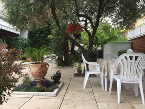 An outdoor patio with white plastic chairs and a table, surrounded by potted plants and a large terracotta pot. - Casa Matilde (Massa)