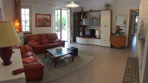 A living room with a sofa, coffee table, and a television. There is a bookshelf and a dining area visible. - Casa Matilde (Massa)