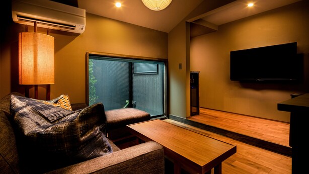 A modern living room with a sofa, a wooden table, a TV mounted on the wall, and an air conditioning unit. - SKY Kyoto (Kyoto)