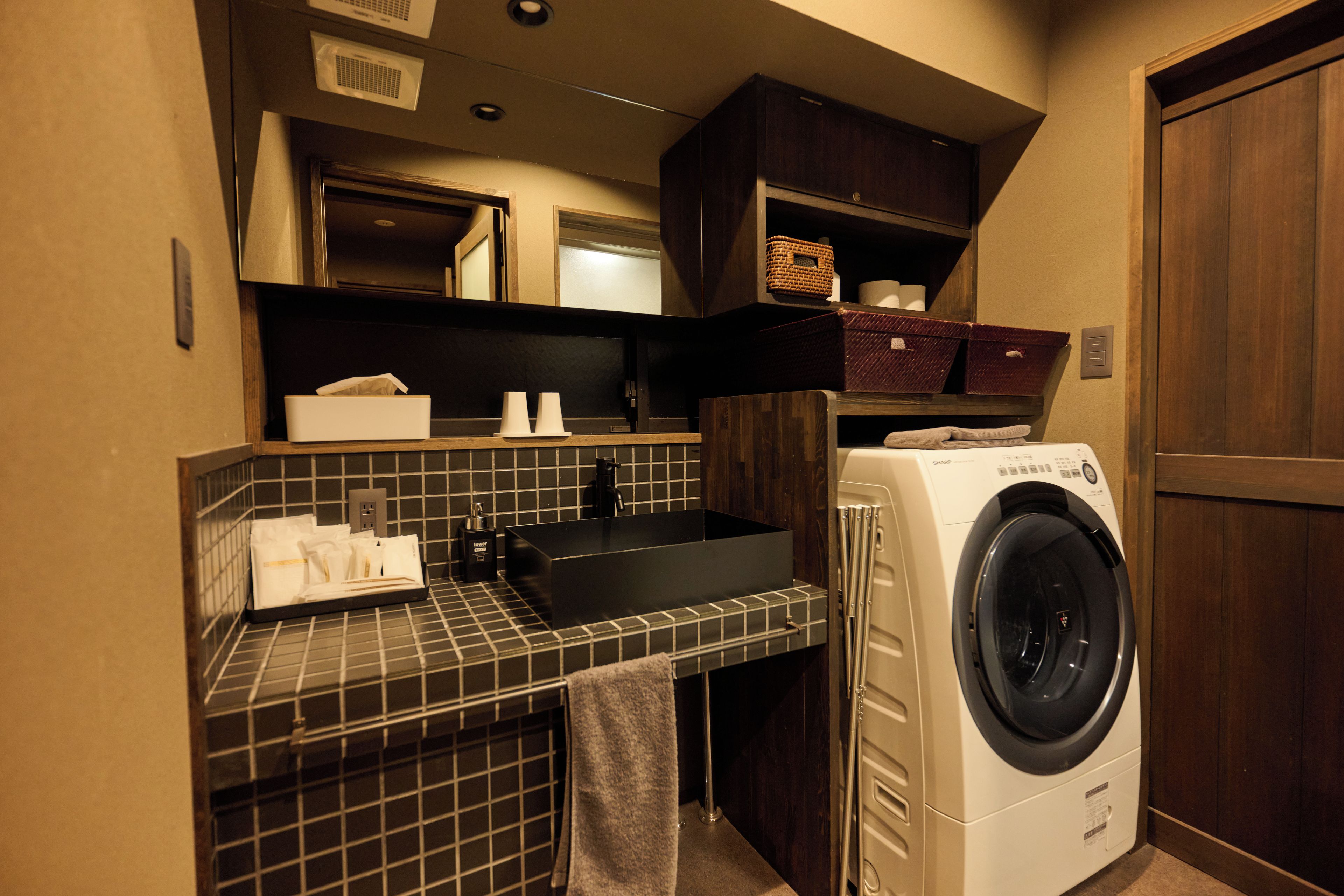 A compact hotel bathroom with a built-in sink, a washing machine, and a towel rack.