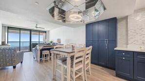 Cocina moderna con comedor, con una lámpara de techo hexagonal, armarios azul oscuro y vistas al océano.