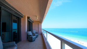 Un balcón con mobiliario de mimbre, una puerta corrediza de vidrio y vista a la playa.