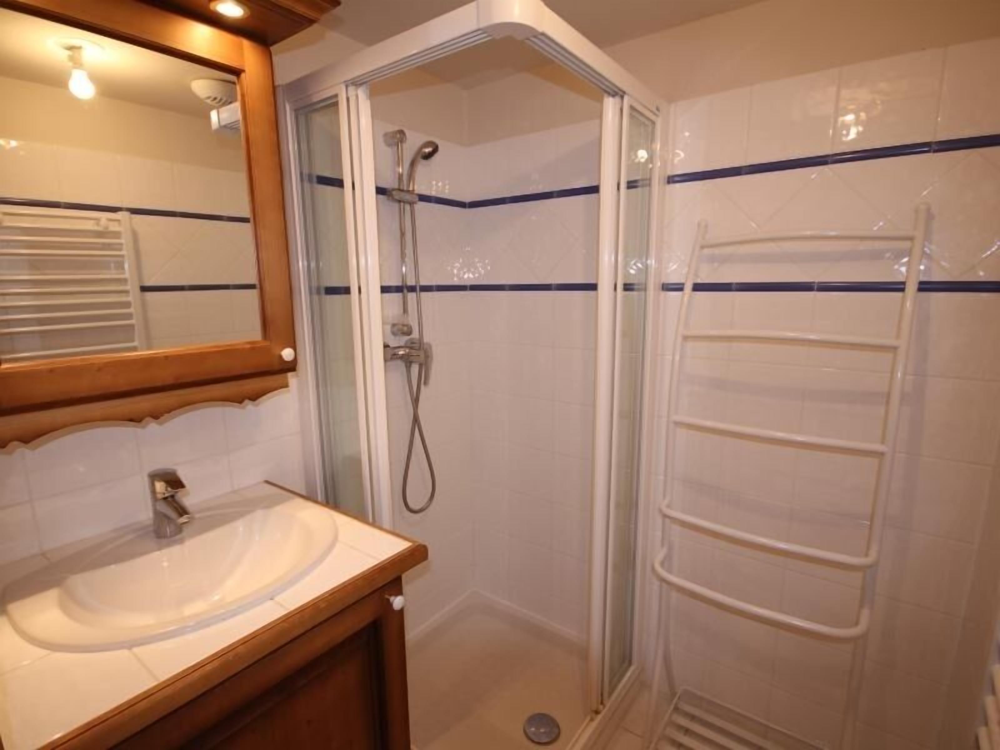 Un baño con ducha envuelta en vidrio, lavamanos con tocador de madera y un perchero para toallas.