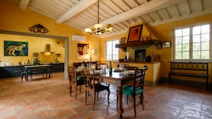 A spacious kitchen with a dining area, featuring a large window, a chandelier, and a tiger painting on the wall. - Villa Bacco (Peccioli)