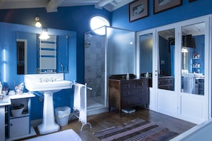 A bathroom with a white sink, a mirror, a wooden cabinet, and a shower area. - Villa Bacco (Peccioli)