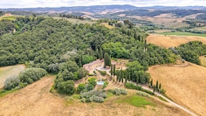 A rural estate with a central building surrounded by dense trees and rolling hills in the background. - Villa Bacco (Peccioli)