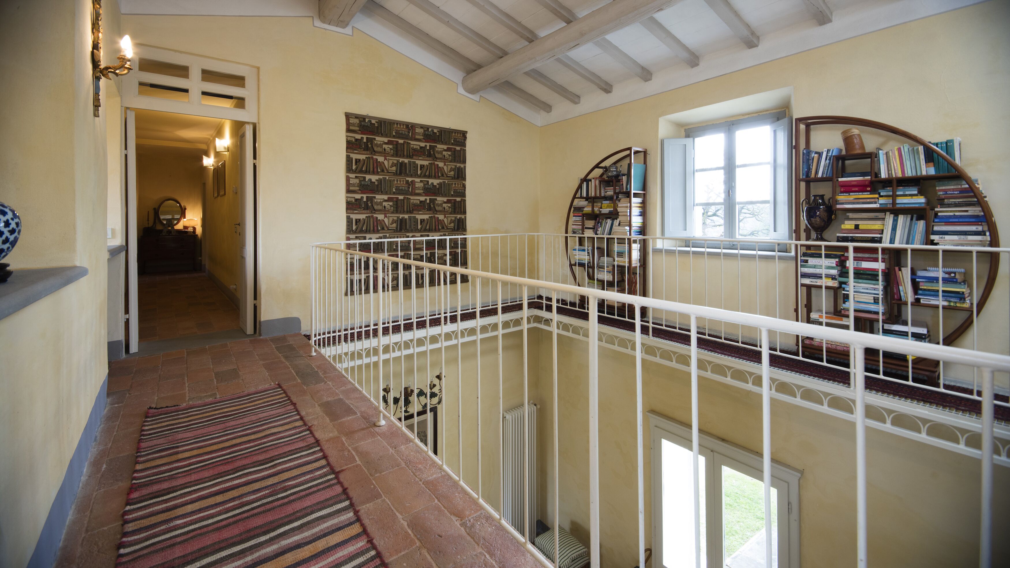 A multi-level interior with a staircase, bookshelves, and a patterned rug.