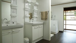 A bathroom with a white sink, mirror, and cabinet, a towel hanging on a rack, and a view of the outside through a door. - Syouyayasikitokura (Kasaoka)