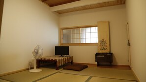 A traditional Japanese room with tatami flooring, a tatami mat table, a television, a standing fan, a wooden cabinet, and a shoji screen. - Syouyayasikitokura (Kasaoka)