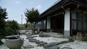 A traditional Japanese building with a wooden exterior, stone steps leading to a wooden door, and a stone lantern in the foreground. - Syouyayasikitokura (Kasaoka)