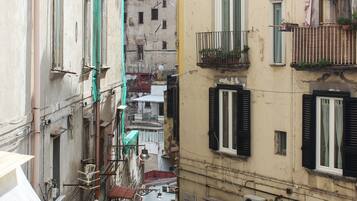 A narrow alleyway between buildings with balconies, potted plants, and outdoor seating.