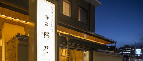 A building with a large illuminated sign in Japanese characters, a covered entrance, and a staircase leading up to the entrance.