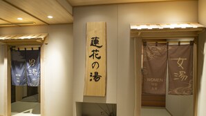 A traditional Japanese room with a wooden sign indicating separate areas for men and women, a small water feature, and a sliding door.