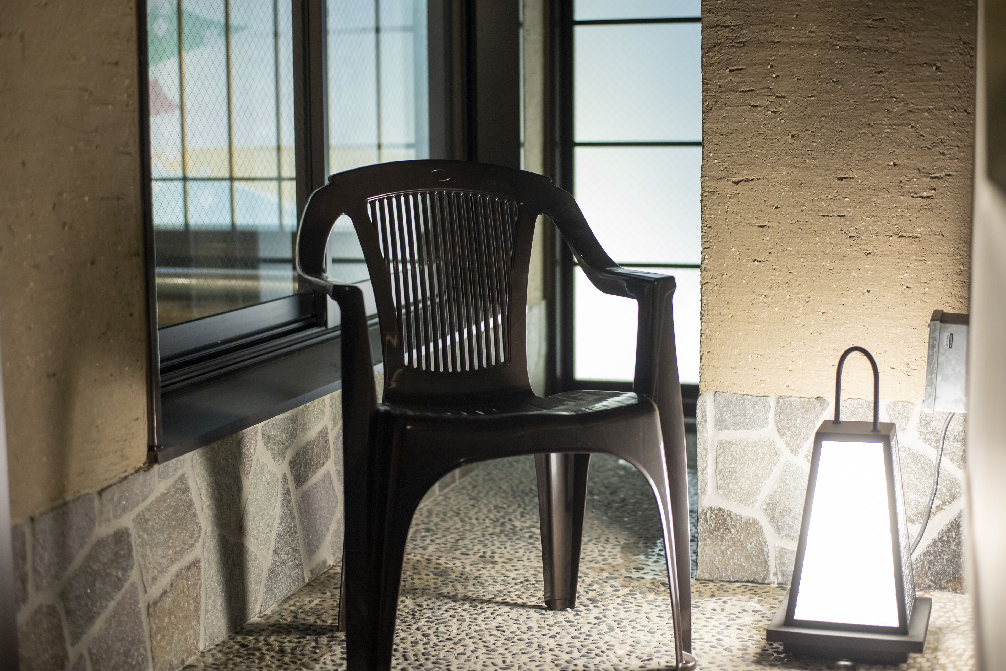 A black plastic chair near a window with a stone wall and a textured wall in the background.