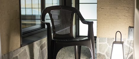 A black plastic chair near a window with a stone wall and a textured wall in the background.