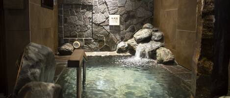 A stone-walled hot tub with a water feature and a clock.