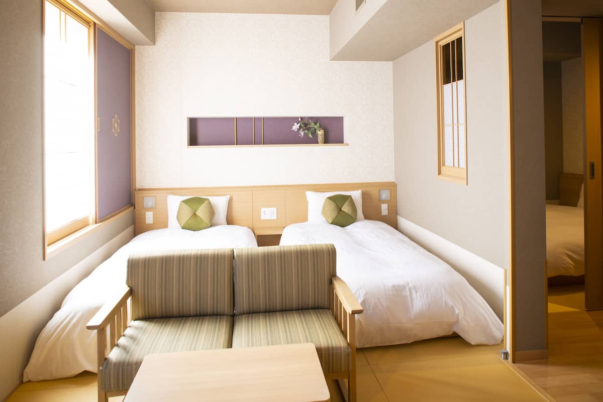 Habitación de hotel con dos camas, un sofá, una mesita y un estante con objetos decorativos.