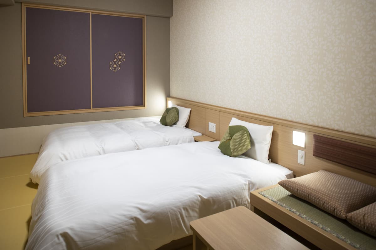 Habitación de hotel con dos camas, cabecero de madera, una mesita pequeña y un armario con diseños geométricos.