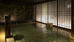An indoor swimming pool with clear water, bamboo plants, and a traditional Japanese-style window with vertical bars.