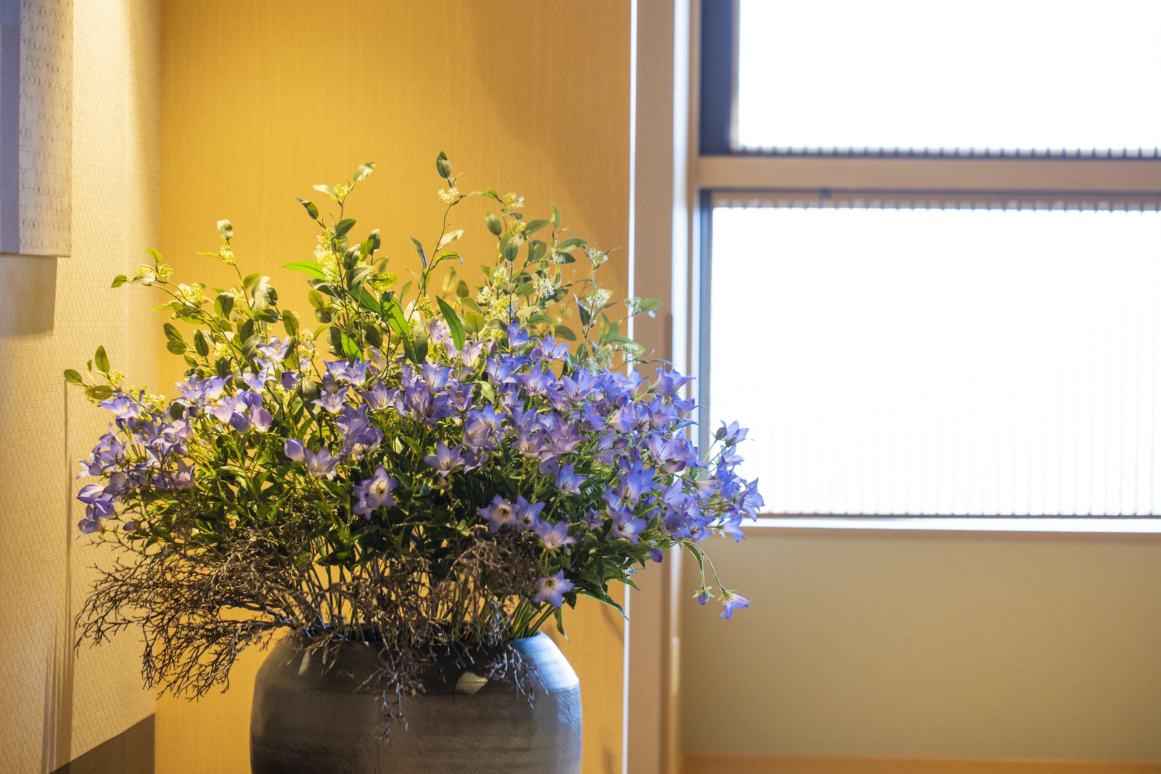 A vase with purple flowers on a table near a window.