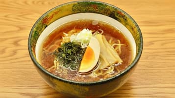 A bowl of ramen with noodles, broth, a soft-boiled egg, and seaweed garnish on a wooden table.