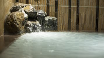 Una fuente de piedra con cascada en una habitación con pared de diseño bambú.