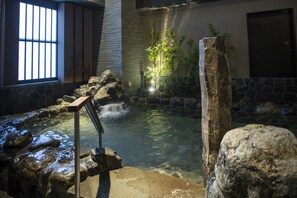A hot spring area with a stone wall, a wooden bench, and a small waterfall.