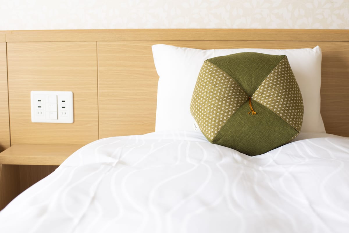 Un lit bien fait, avec une couette blanche et un oreiller à motifs verts et blancs.