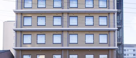 Un hotel de varios pisos con fachada plana, múltiples ventanas por planta y una entrada visible con un letrero.