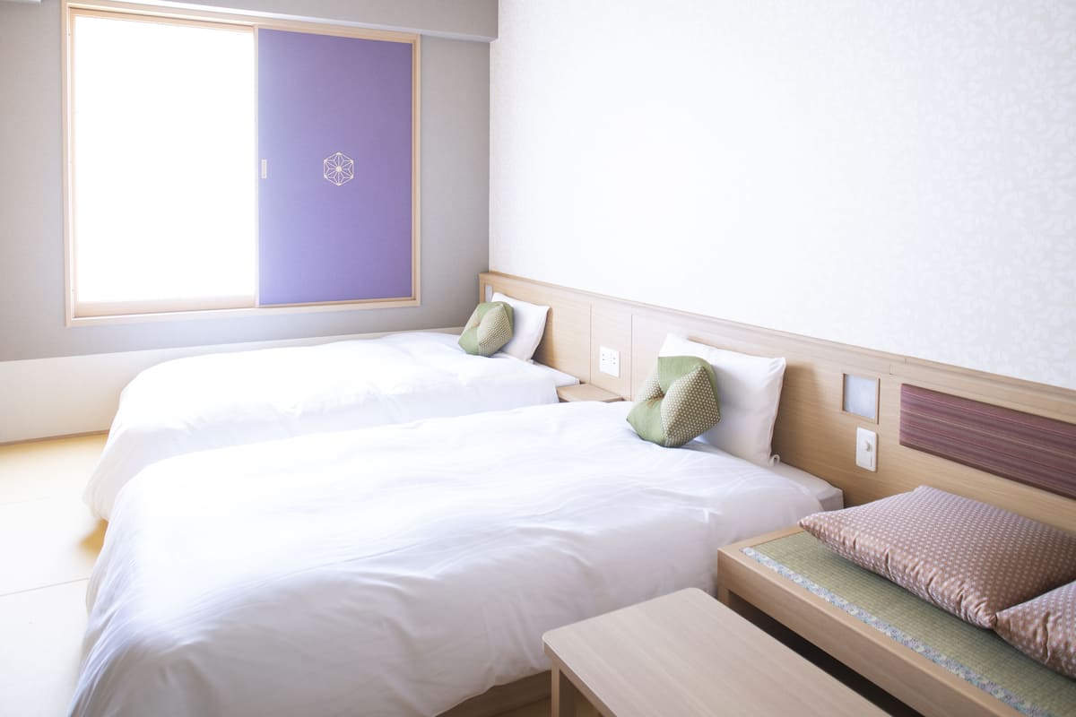Une chambre d’hôtel avec deux lits, une petite table et une fenêtre donnant sur un paysage agréable.
