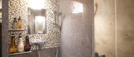 A bathroom with a tiled shower area, a sink with a mirror, and toiletries on a shelf.